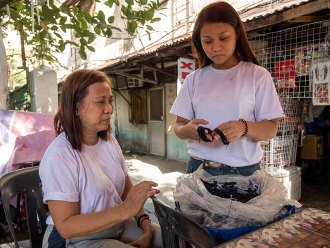 Esther Co Yu (seated) and daughter Gwyneth look at the excess elastic bands of sports socks that they use to weave rugs and seat covers for Tzu Chi’s livelihood program. 【Photo by Harold Alzaga】