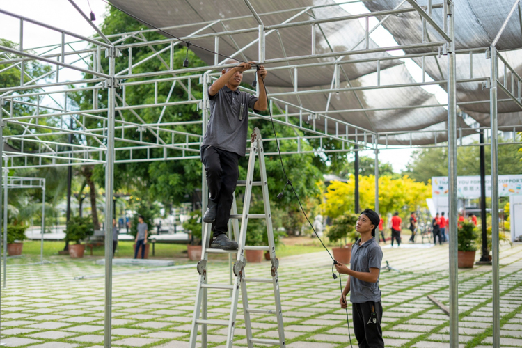 A Tzu Chi staffer installs a dangling light bulb socket on a canopy beam. 