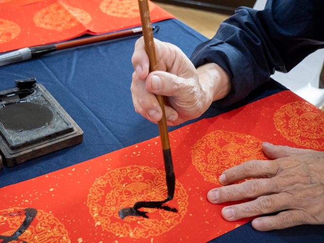 Chinese calligraphers stationed by the entrance of Jing Si Auditorium hand-write auspicious messages in scrolls for guests to hang in their homes. 