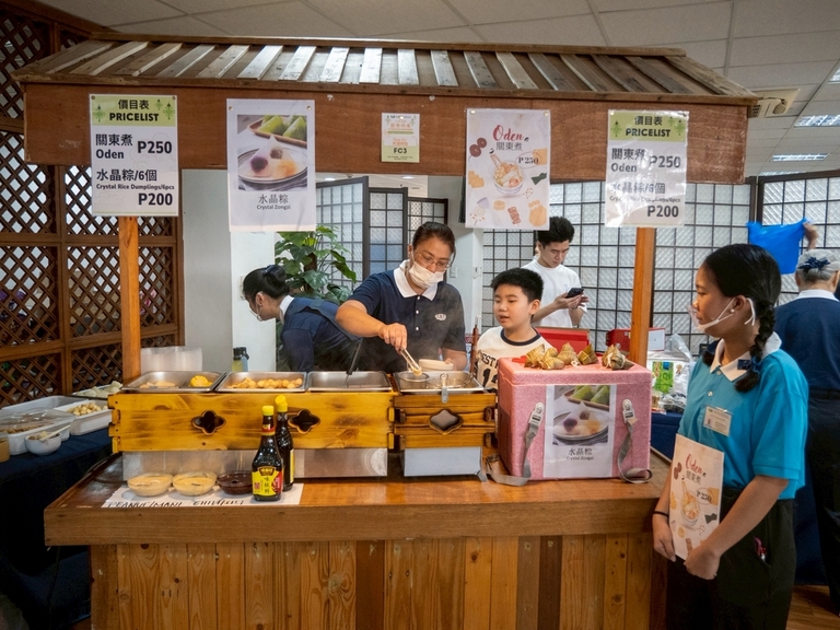 A young boy and Tzu Chi scholar watch as a volunteer prepares a bowl of oden, a soup loaded with ingredients.