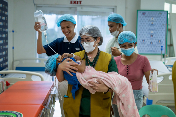 Tzu Chi Zamboanga volunteer Harvey Yap (back left, in blue) and mother Norvelyn Rivas (right in pink) cannot contain their joy following the herniorrhaphy of Rivas’ daughter Yeshaa Brianna Puda (carried by a Tzu Chi volunteer). “Thank you, because the Lord used you as a way for my daughter to get better,” says Rivas.