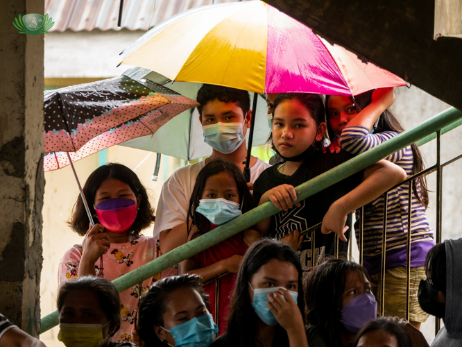 Young beneficiaries take cover under umbrellas during a visit from Tzu Chi volunteers on a rainy day. 