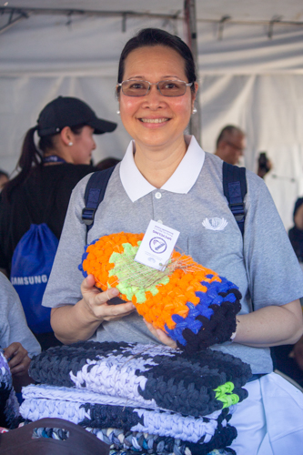 At the Tzu Chi booth of Runrio’s Galaxy Watch Earth Day Run, volunteer Joy Gatdula shows one of the upcycled items for sale, a mat woven from the excess material of sports socks. 【Photo by Matt Serrano】