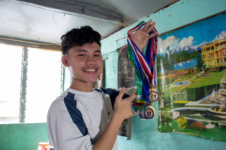 John Gabriel Zarceno shows the medals he’s received from school. Despite parttime jobs as a manicurist, choreographer, and event host, he is a longtime student leader and advocate of children’s rights. 【Photo by Marella Saldonido】