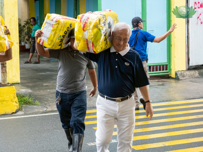 Tzu Chi volunteer James Cheng (right) helps carry the sacks of face masks to the schools for distribution.