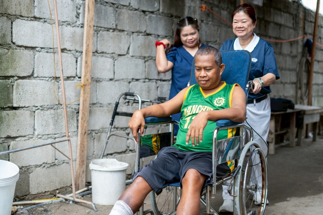 Tzu Chi volunteer Jocie Chua pushes Levy Telecio in a wheelchair provided by the foundation. The wheelchair allows him to move around more easily on his own, especially during times when he is left at home while his wife, Venus, is at work.
