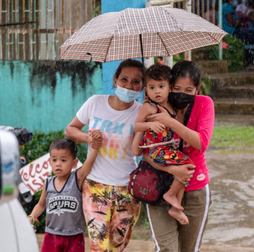 Women and their children try to keep dry under one umbrella. 