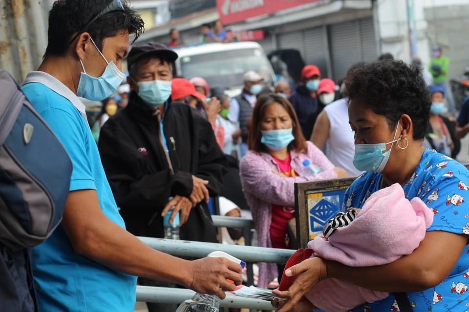 A woman holds her baby as her hands are sprayed before she enters the bank. 