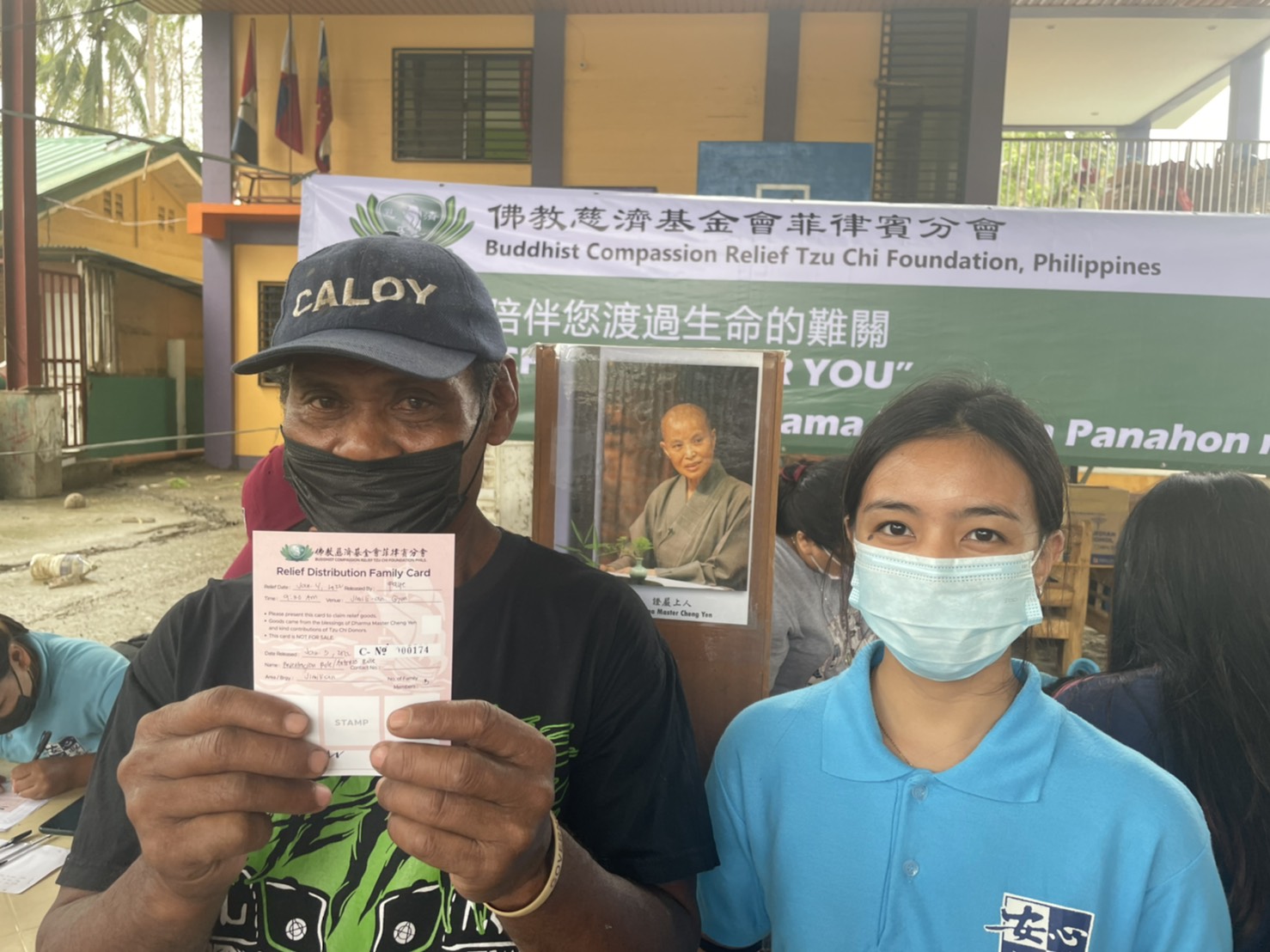 A beneficiary from Barangay Jimilian holds up his relief card while posing with a Tzu Chi scholar. 