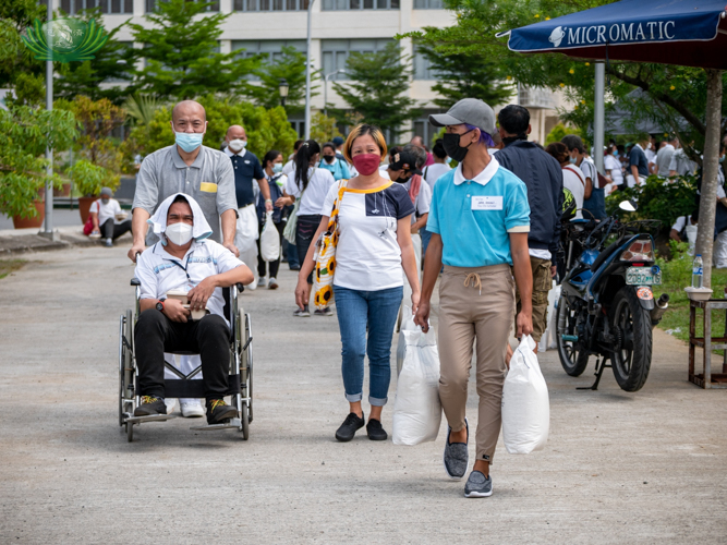 Tzu Chi volunteer and scholar assist beneficiaries in carrying their rice and groceries.【Photo by Daniel Lazar】