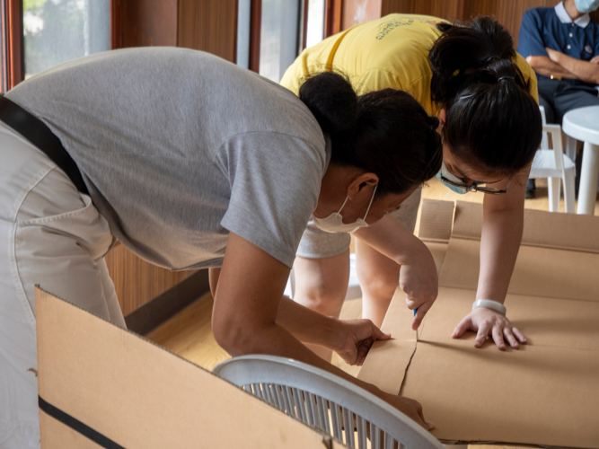 Volunteer Nathania Tan (in yellow) cuts the cardboard sourced from Tzu Chi’s recycling center. “We experimented with a lot of materials and every time we made adjustments we always failed,” says the graphic artist from the Office of the CEO. “Though my teammates and I were very discouraged, our perseverance and the encouragement of Tzu Chi volunteers helped us push through despite our struggles.”【Photo by Matt Serrano】