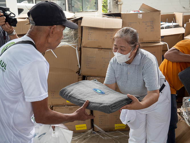 Tzu Chi volunteer hands a blanket over to a beneficiary. 【Photo by Matt Serrano】