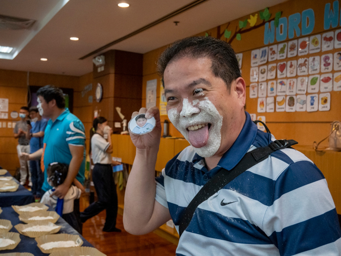In the flour game, fathers attempt to find a hidden photo of their children in a plate full of flour using only their face. 【Photo by Harold Alzaga】