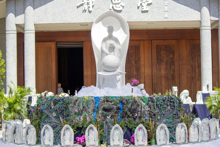 A big Buddha statue adorned with flowers, greenery, and crystal Buddhas stands on the main Buddha bathing table.