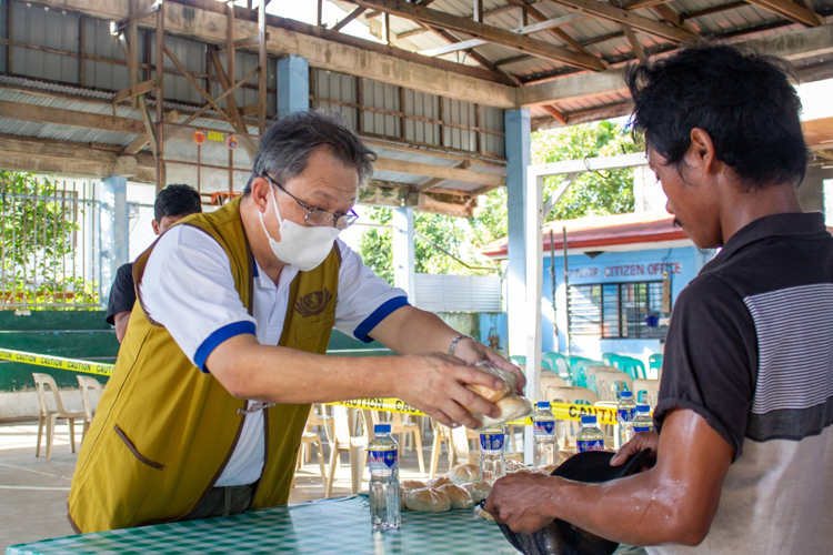 Mr. Paulino Ang, a volunteer from Cauayan, Isabela, hands a bread snack to a beneficiary. 【Photo by Marella Saldonido】